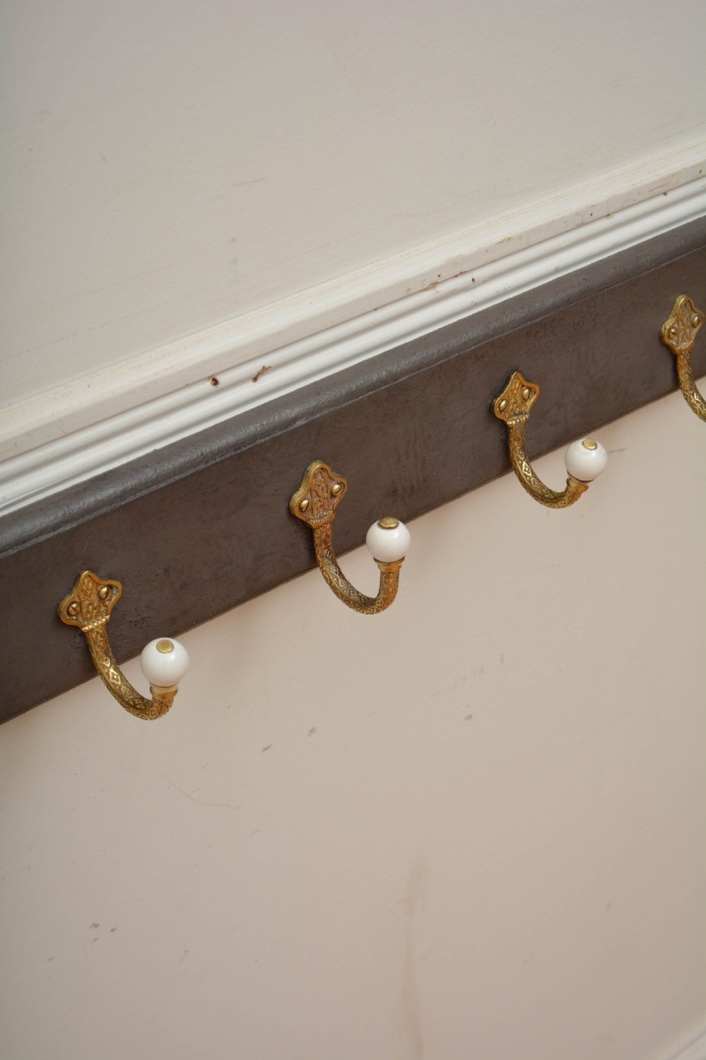 A wall-mounted grey wooden rail fitted with multiple cast brass coat hooks featuring white ceramic ball tips. View IV