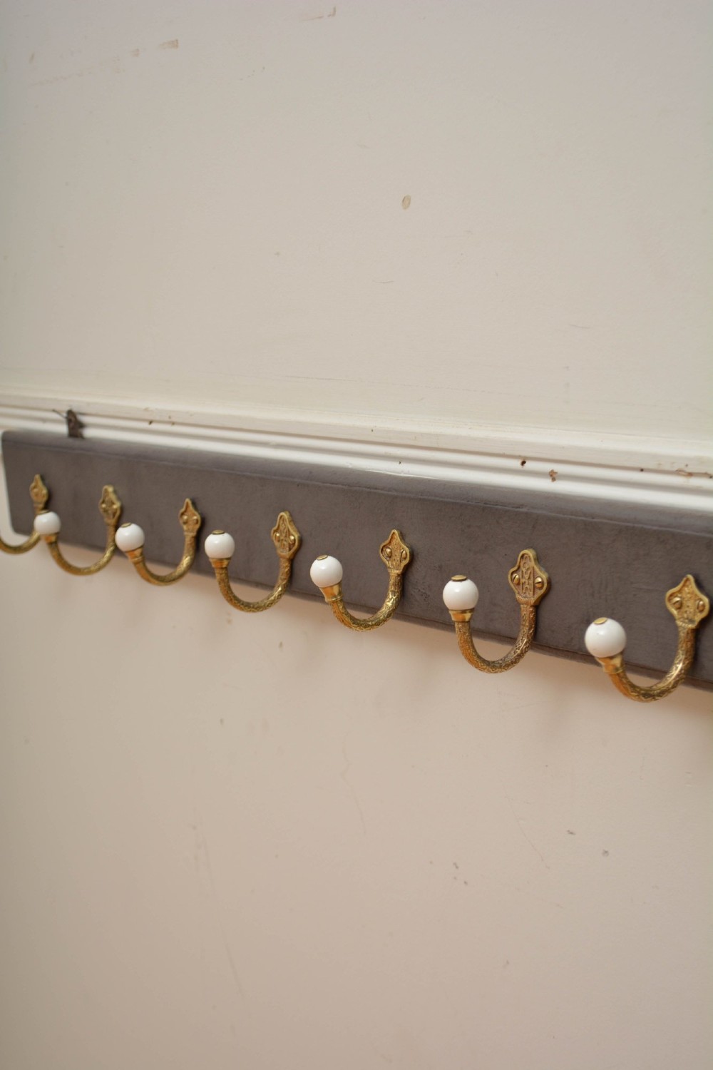 A wall-mounted grey wooden rail fitted with multiple cast brass coat hooks featuring white ceramic ball tips.