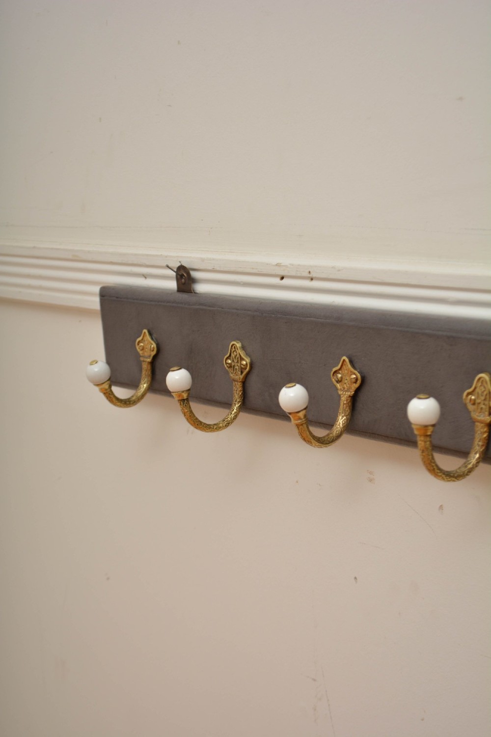 A wall-mounted grey wooden rail fitted with multiple cast brass coat hooks featuring white ceramic ball tips. View VII