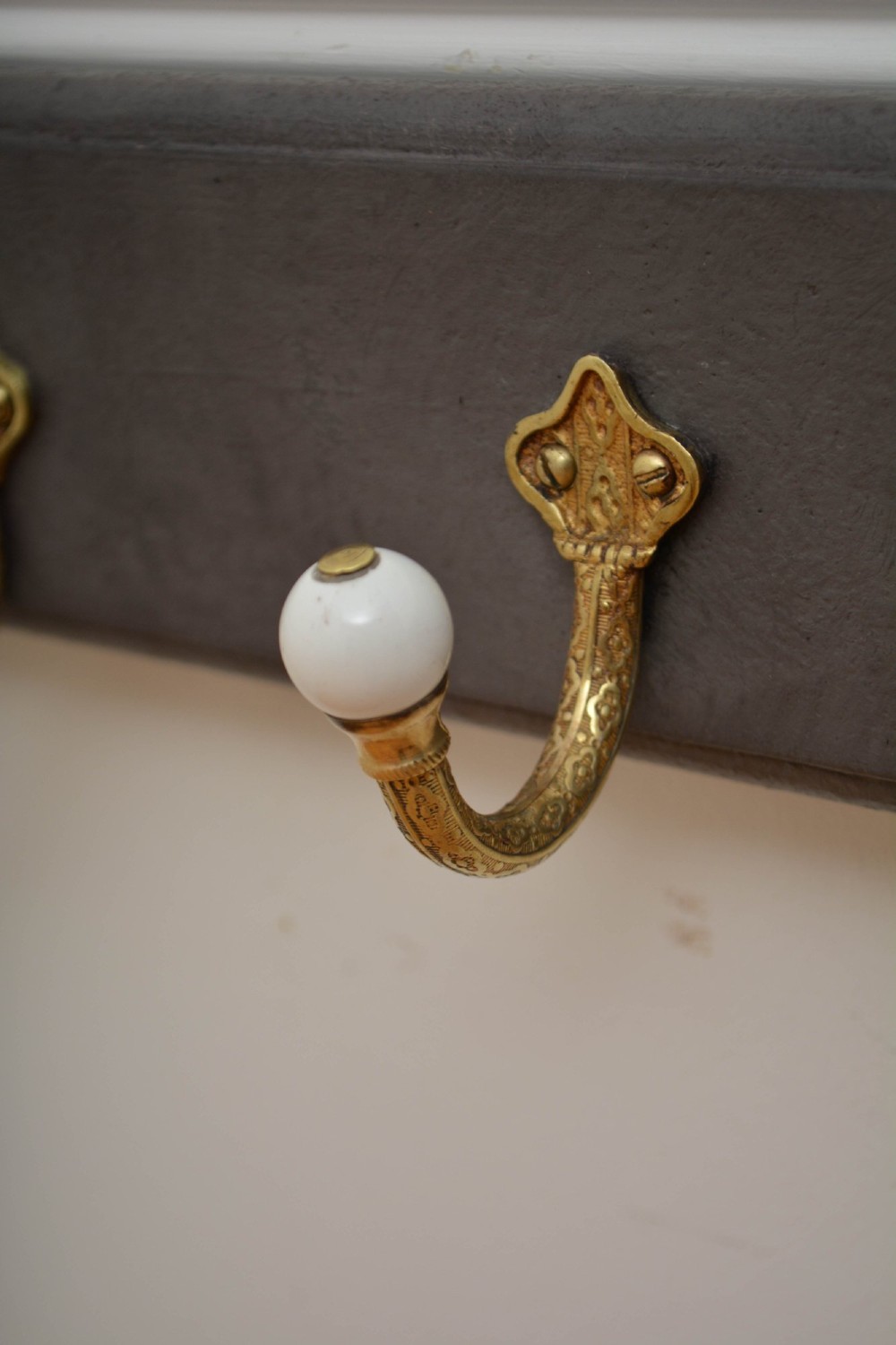 A wall-mounted grey wooden rail fitted with multiple cast brass coat hooks featuring white ceramic ball tips. View VIII