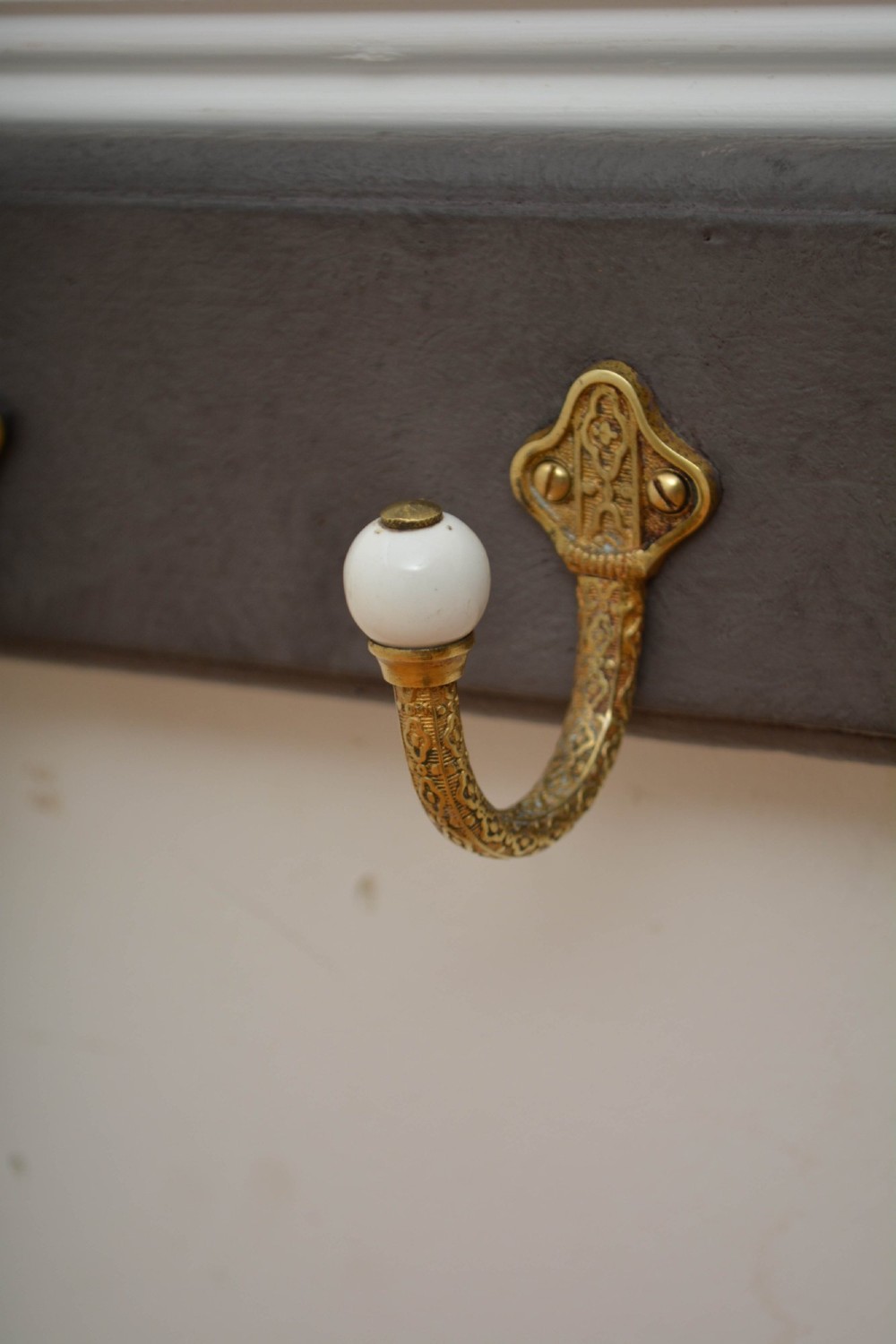A wall-mounted grey wooden rail fitted with multiple cast brass coat hooks featuring white ceramic ball tips. View IX