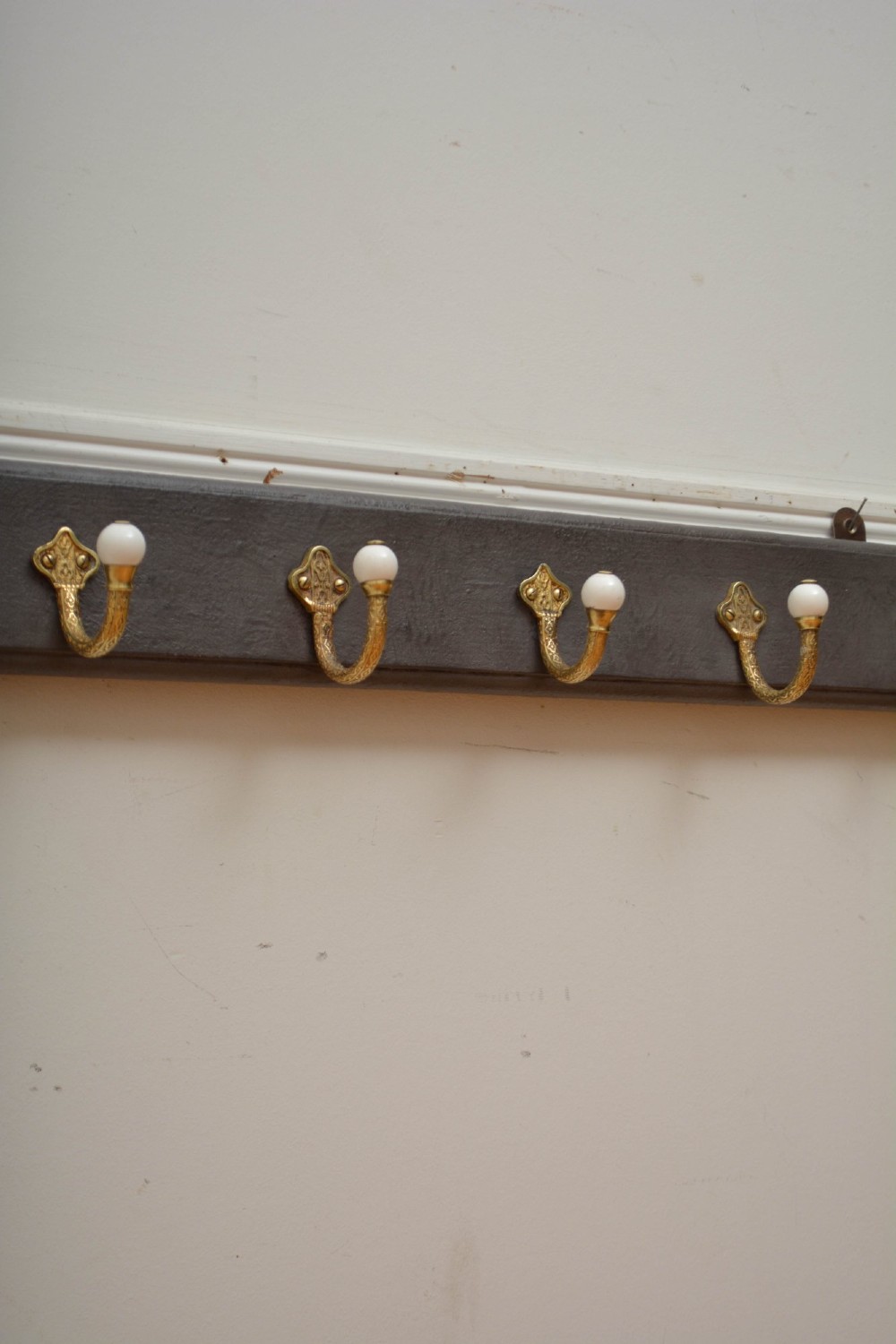 A wall-mounted grey wooden rail fitted with multiple cast brass coat hooks featuring white ceramic ball tips. View XI
