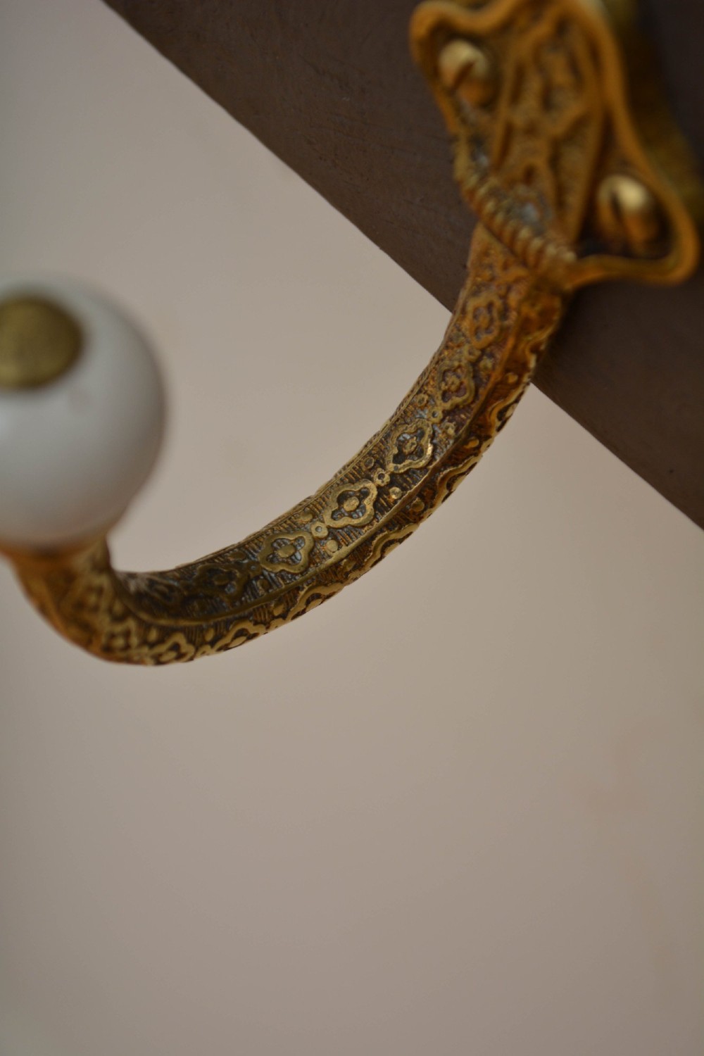 A wall-mounted grey wooden rail fitted with multiple cast brass coat hooks featuring white ceramic ball tips. View XII