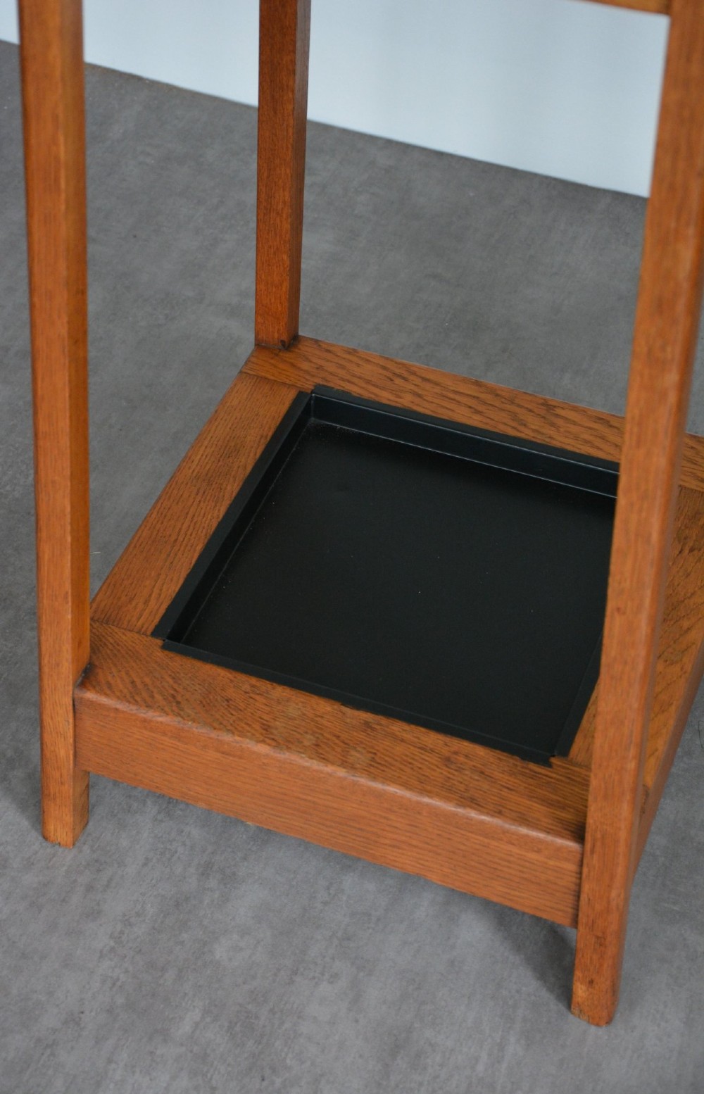 A tall tapered oak coat and umbrella stand featuring top metal hooks, an intermediate square divider, and a dark metal drip tray at the base. View II