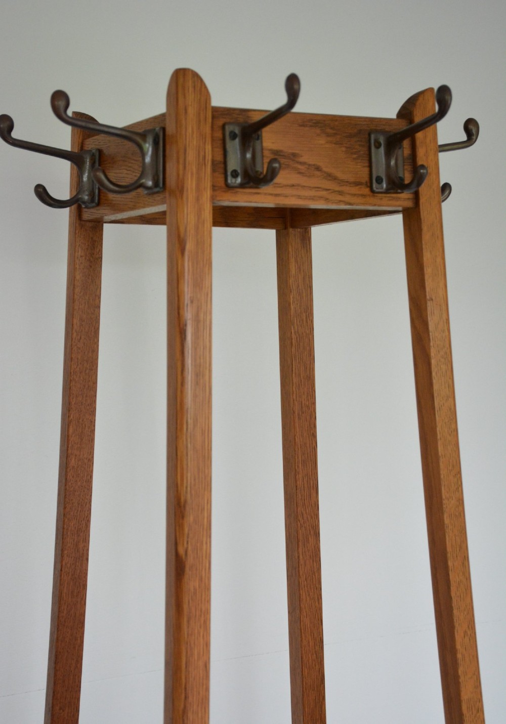 A tall tapered oak coat and umbrella stand featuring top metal hooks, an intermediate square divider, and a dark metal drip tray at the base. View VI
