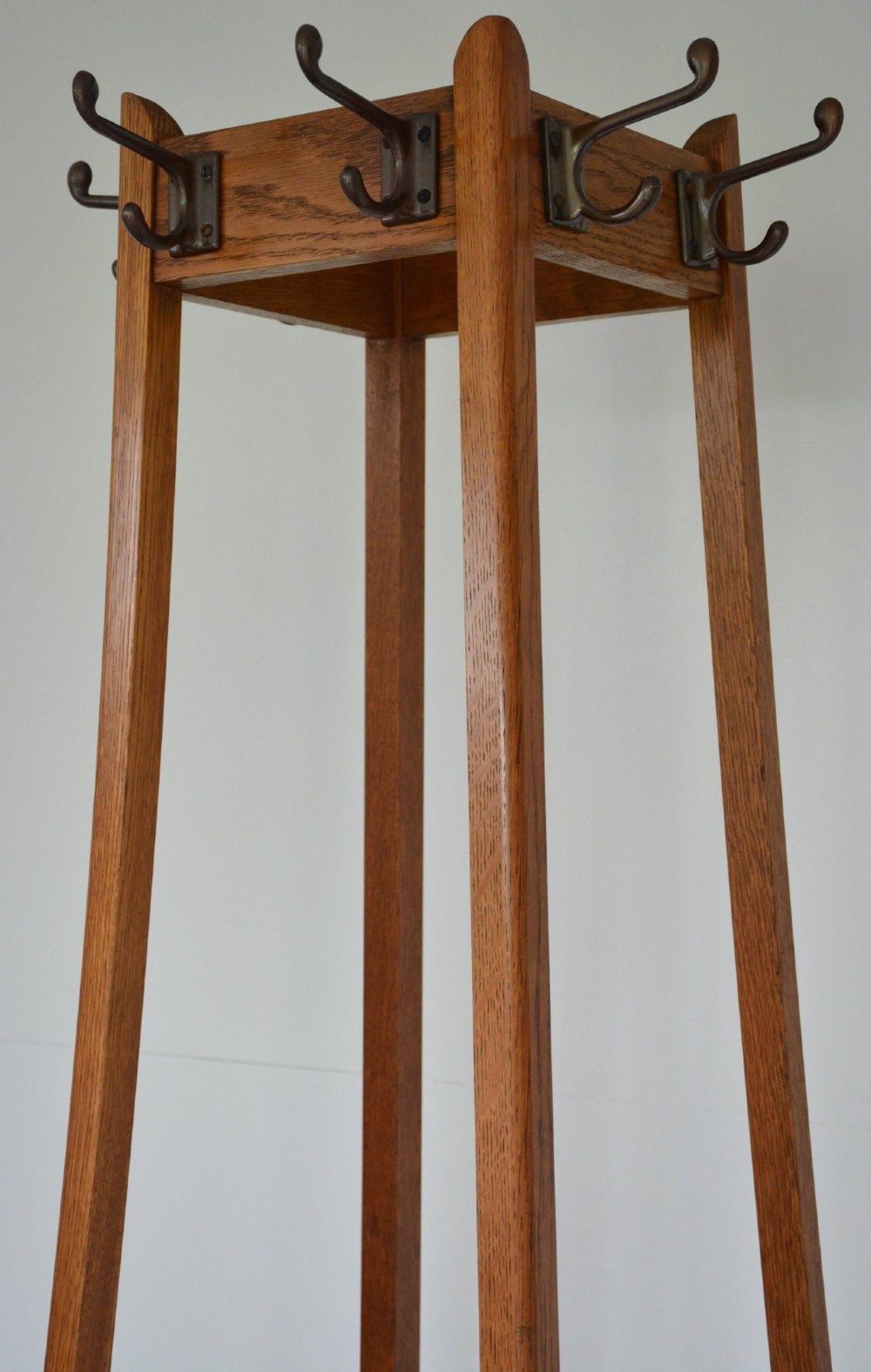 A tall tapered oak coat and umbrella stand featuring top metal hooks, an intermediate square divider, and a dark metal drip tray at the base. View VII