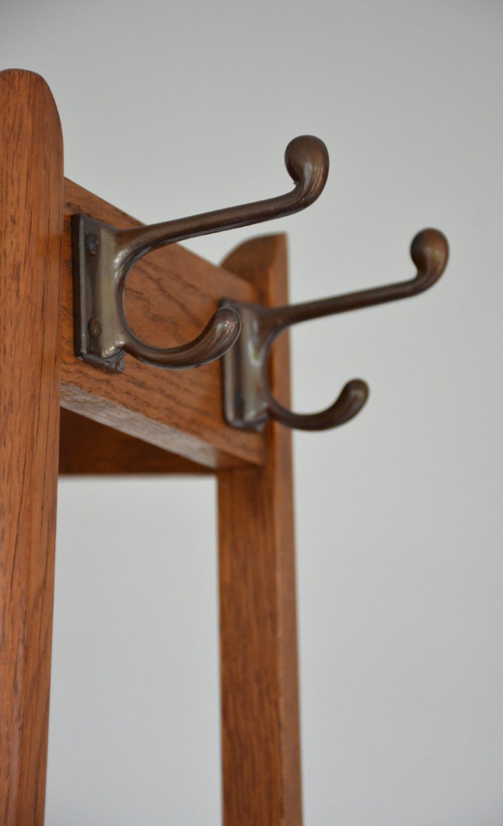 A tall tapered oak coat and umbrella stand featuring top metal hooks, an intermediate square divider, and a dark metal drip tray at the base. View IX
