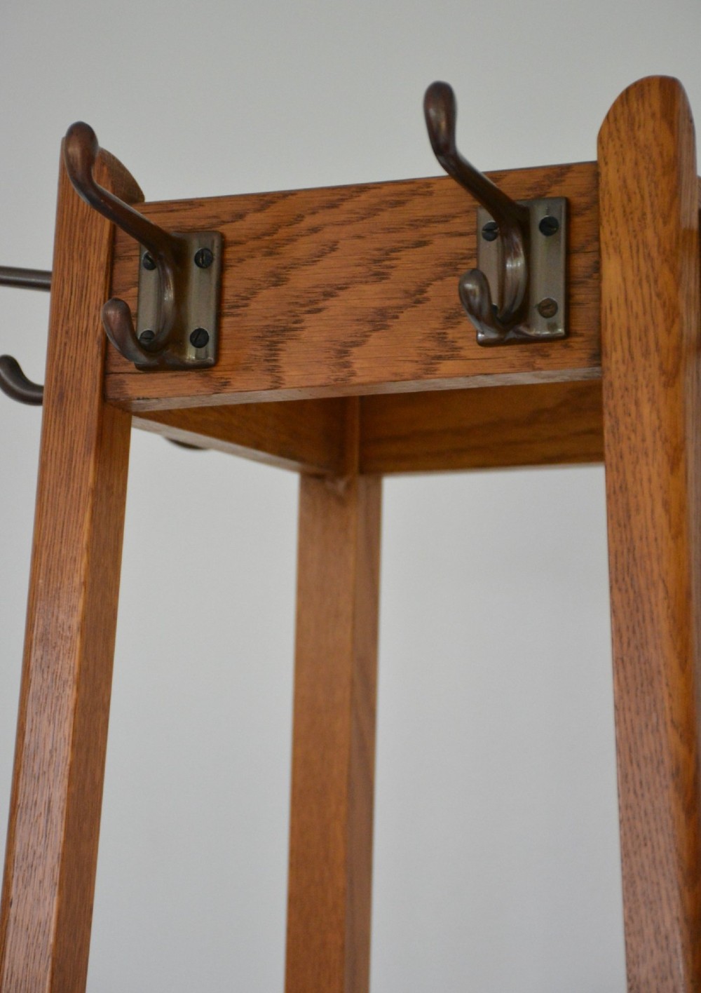 A tall tapered oak coat and umbrella stand featuring top metal hooks, an intermediate square divider, and a dark metal drip tray at the base. View XI