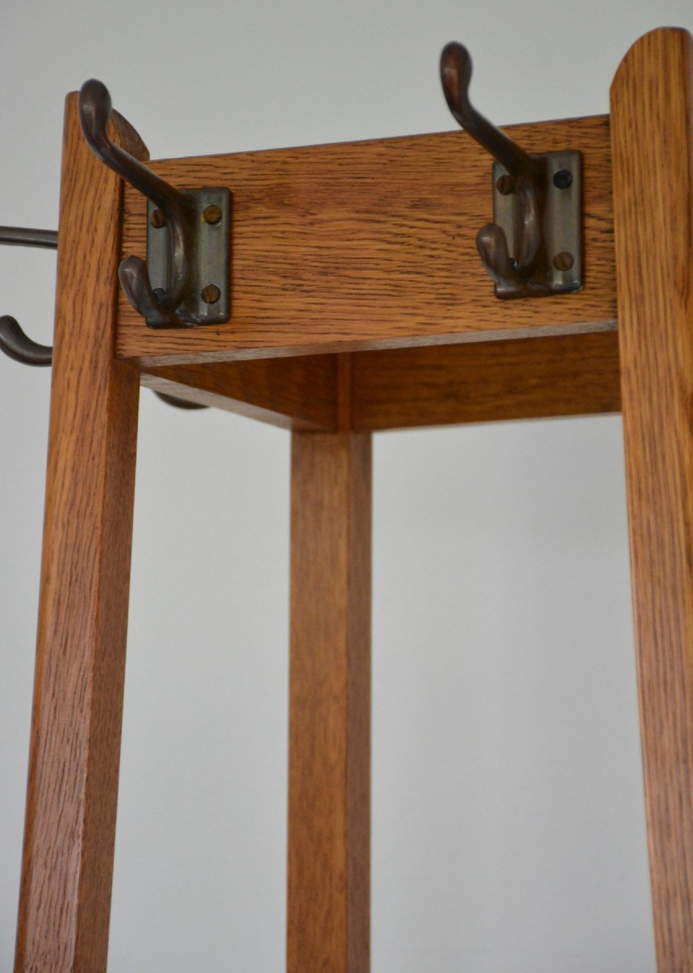 A tall tapered oak coat and umbrella stand featuring top metal hooks, an intermediate square divider, and a dark metal drip tray at the base. View XII