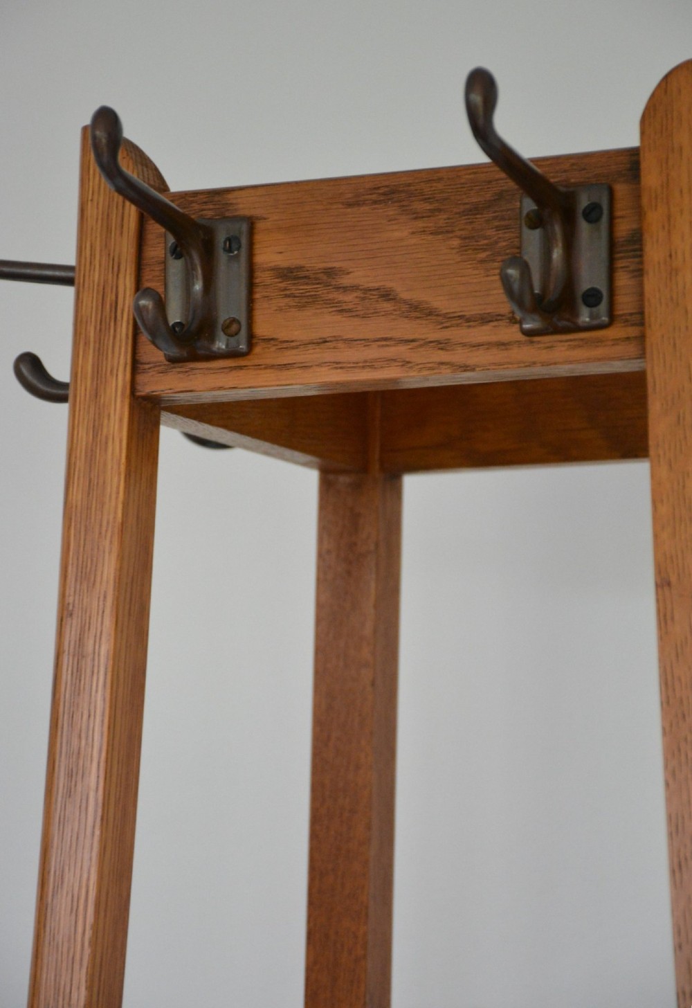 A tall tapered oak coat and umbrella stand featuring top metal hooks, an intermediate square divider, and a dark metal drip tray at the base. View XIII