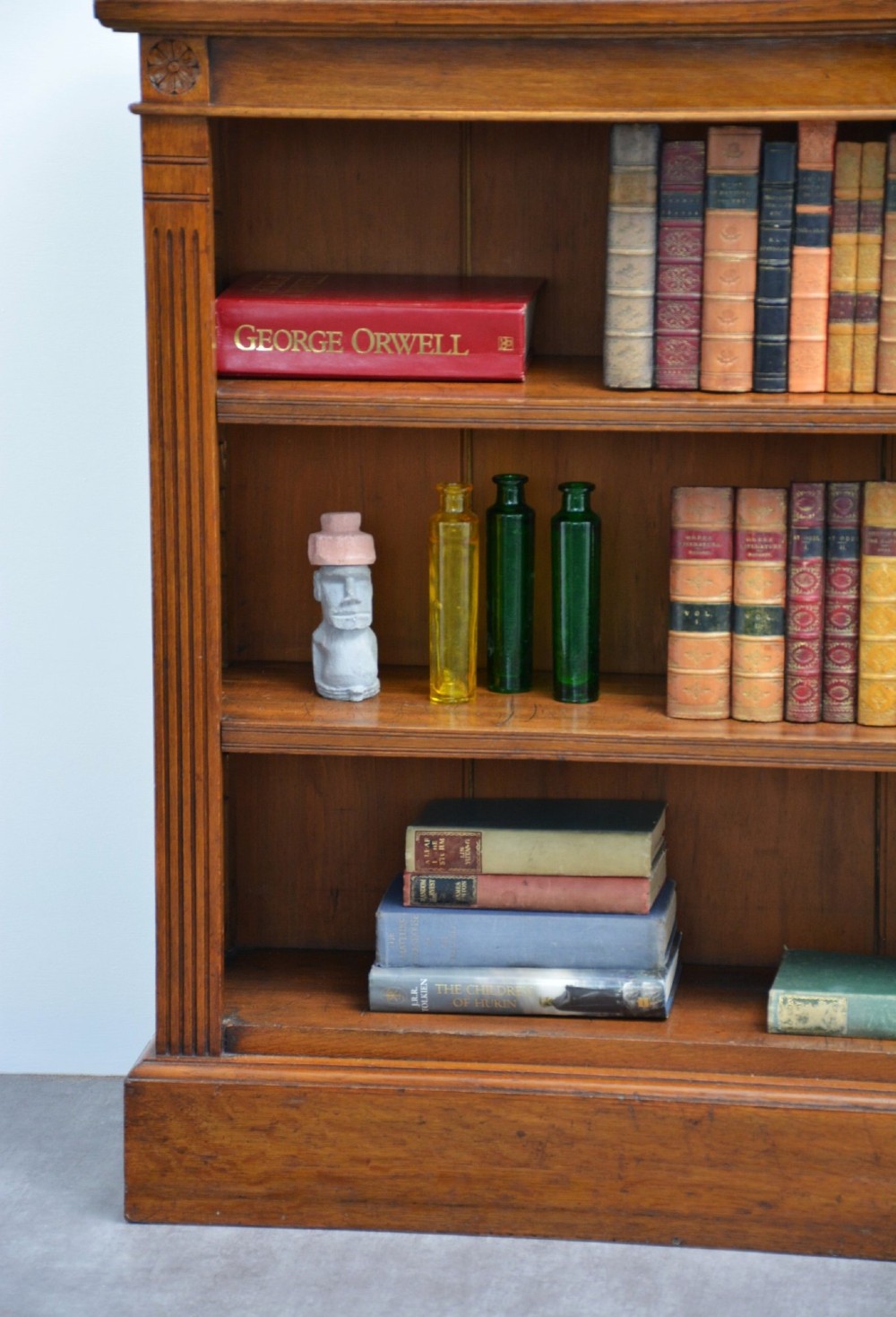 A late Victorian low solid oak open bookcase featuring three horizontal shelves, fluted pilasters, and carved corner rosettes. View V