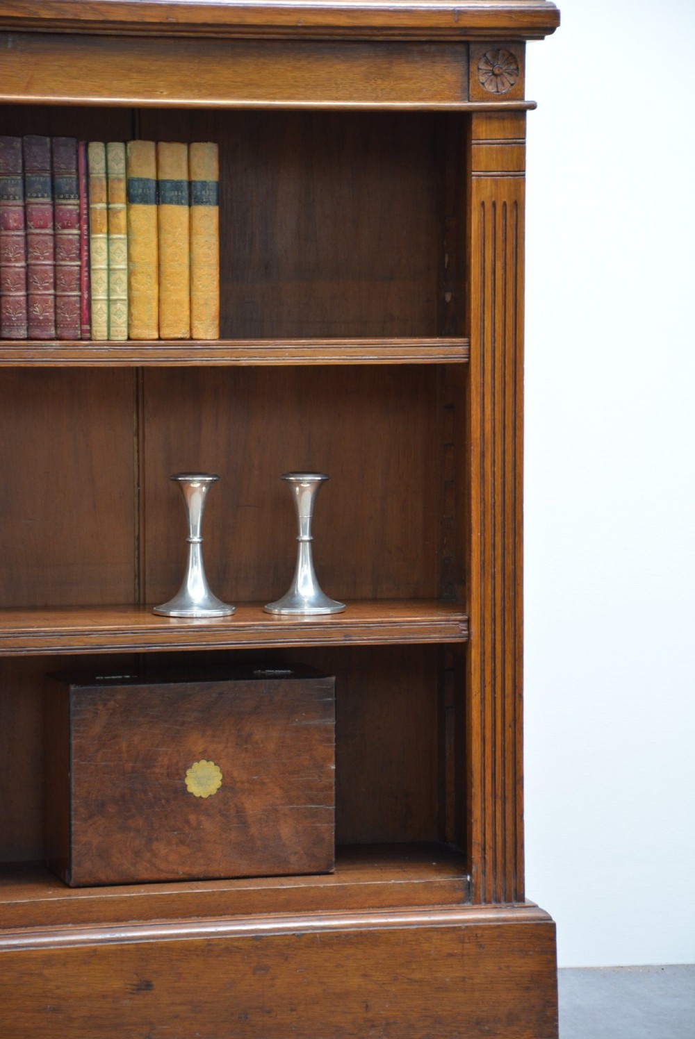 A late Victorian low solid oak open bookcase featuring three horizontal shelves, fluted pilasters, and carved corner rosettes. View VI