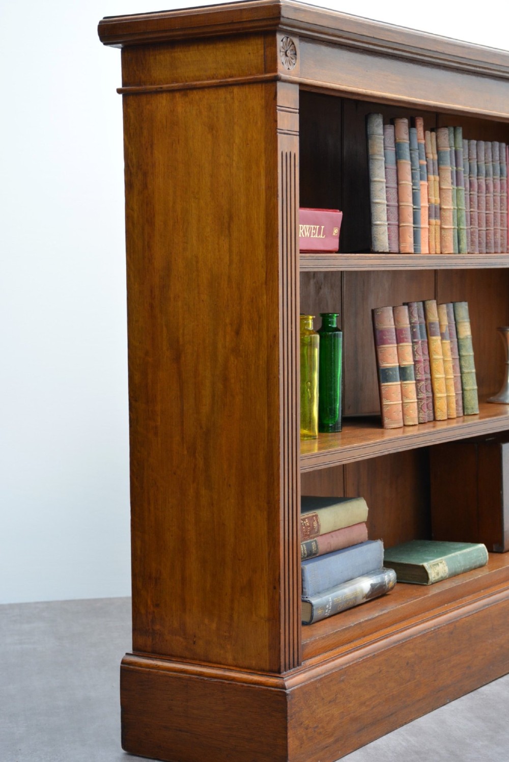 A late Victorian low solid oak open bookcase featuring three horizontal shelves, fluted pilasters, and carved corner rosettes. View VII
