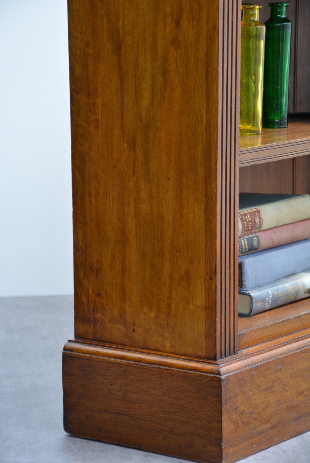 A late Victorian low solid oak open bookcase featuring three horizontal shelves, fluted pilasters, and carved corner rosettes. View IX