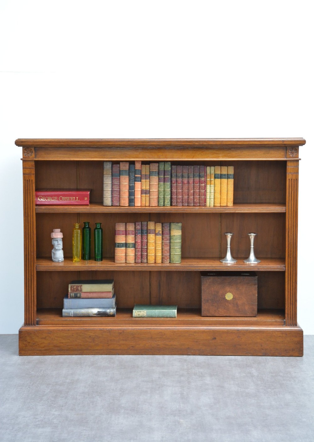 A late Victorian low solid oak open bookcase featuring three horizontal shelves, fluted pilasters, and carved corner rosettes.