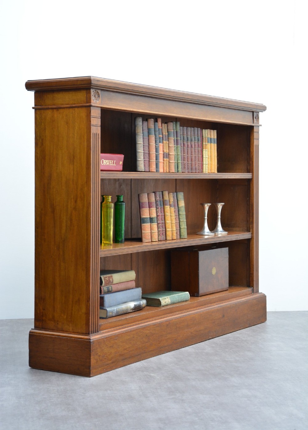 A late Victorian low solid oak open bookcase featuring three horizontal shelves, fluted pilasters, and carved corner rosettes. View XIII