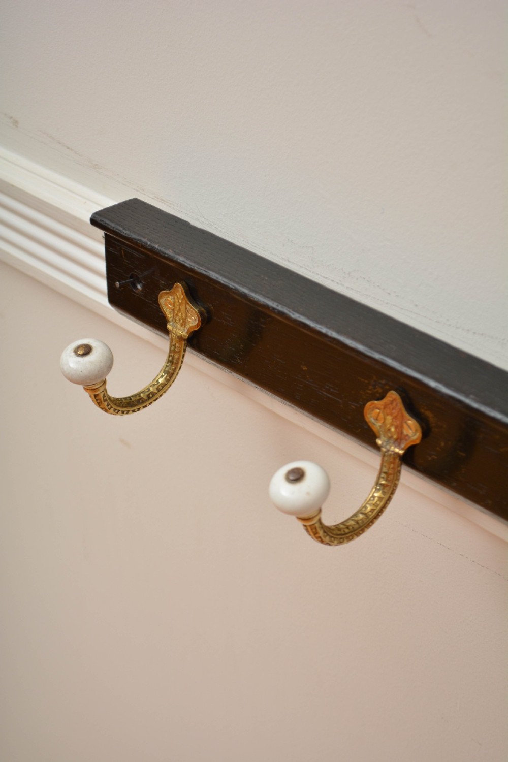 An ebonised solid oak wall rack featuring four decorative cast brass hooks topped with white ceramic knobs. View XII