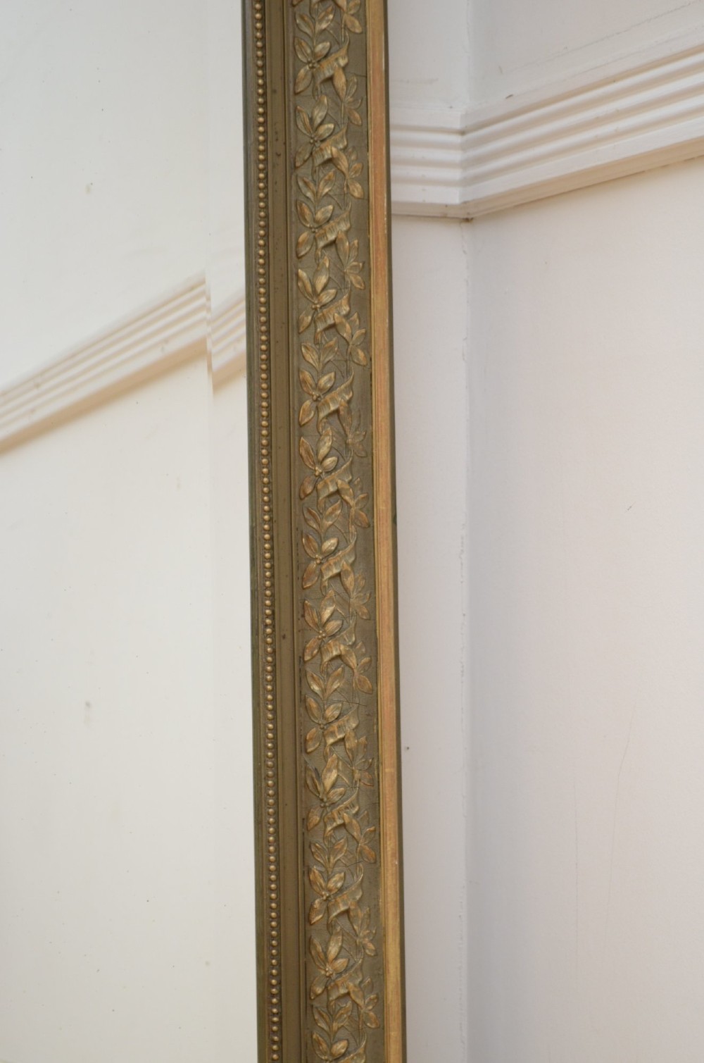 A large rectangular French wall mirror featuring a gilded wood frame, an olive green painted frieze decorated with carved floral swags, and an ornate ribbon bow crest. View VII