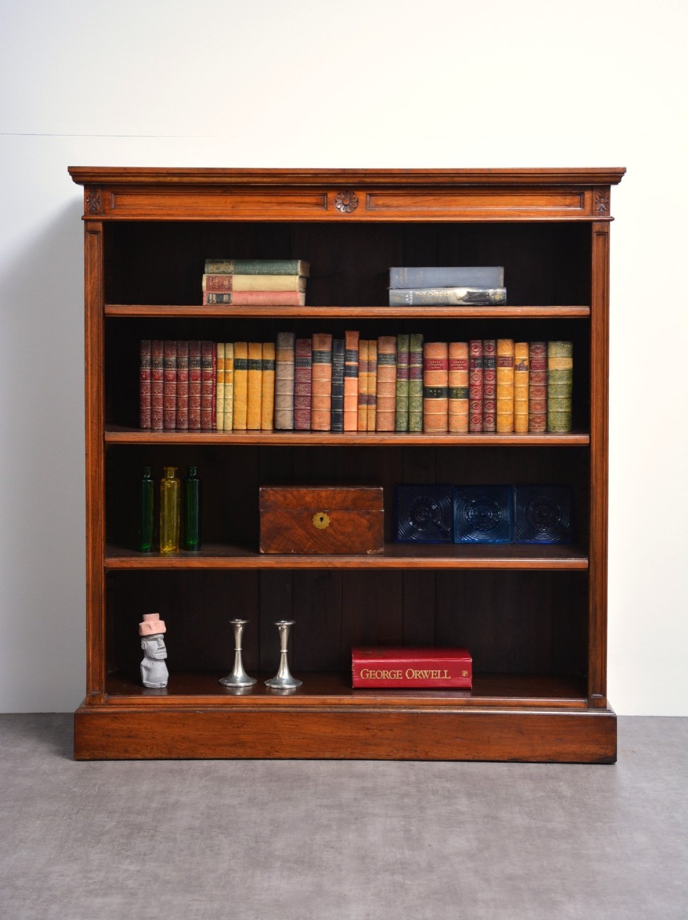A late Victorian open walnut bookcase featuring a carved rosette frieze, moulded top cornice, adjustable shelves, and a solid plinth base.