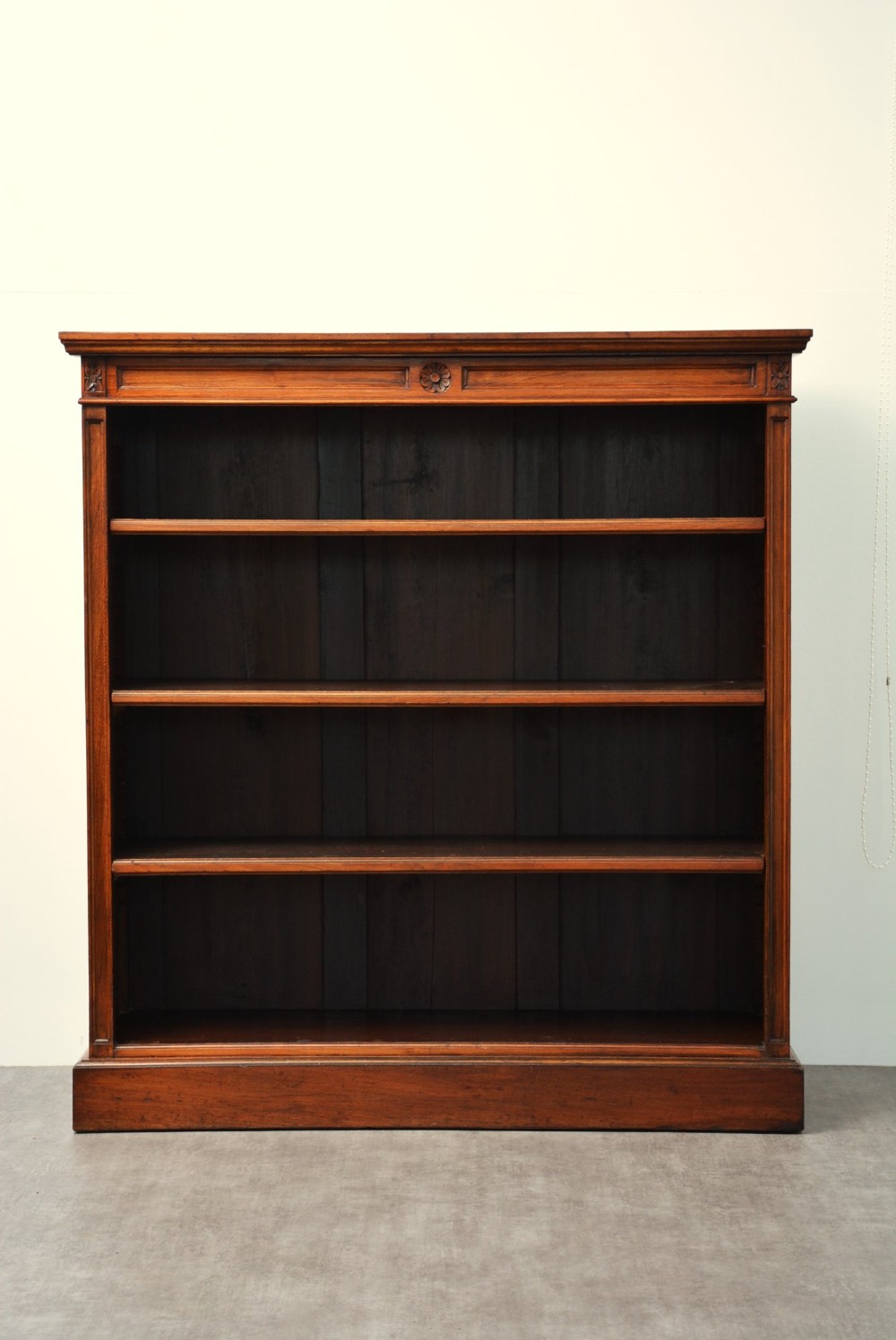 A late Victorian open walnut bookcase featuring a carved rosette frieze, moulded top cornice, adjustable shelves, and a solid plinth base. View VII