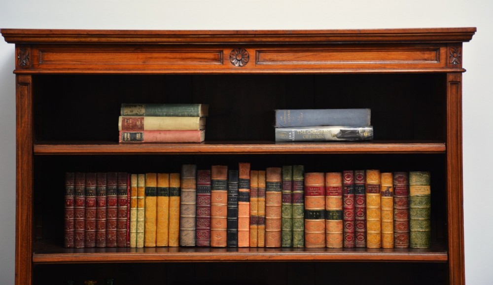 A late Victorian open walnut bookcase featuring a carved rosette frieze, moulded top cornice, adjustable shelves, and a solid plinth base. View IX