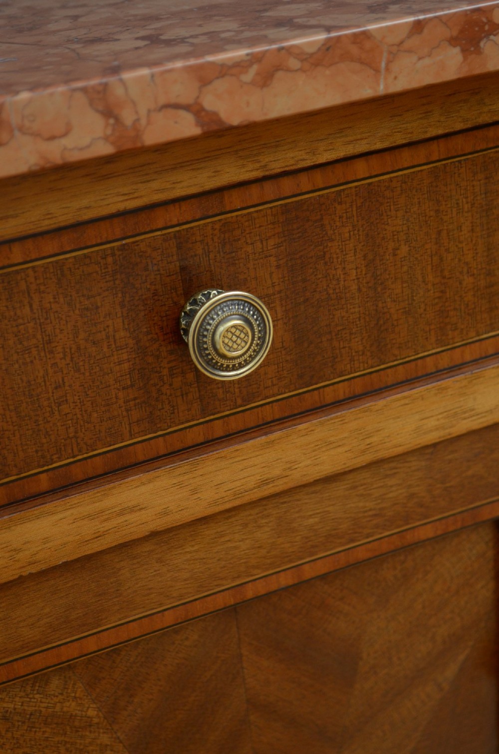 A matching pair of French mahogany bedside cabinets featuring pink marble tops, single drawers over small cupboards with sunburst parquetry, and slender turned legs. View V