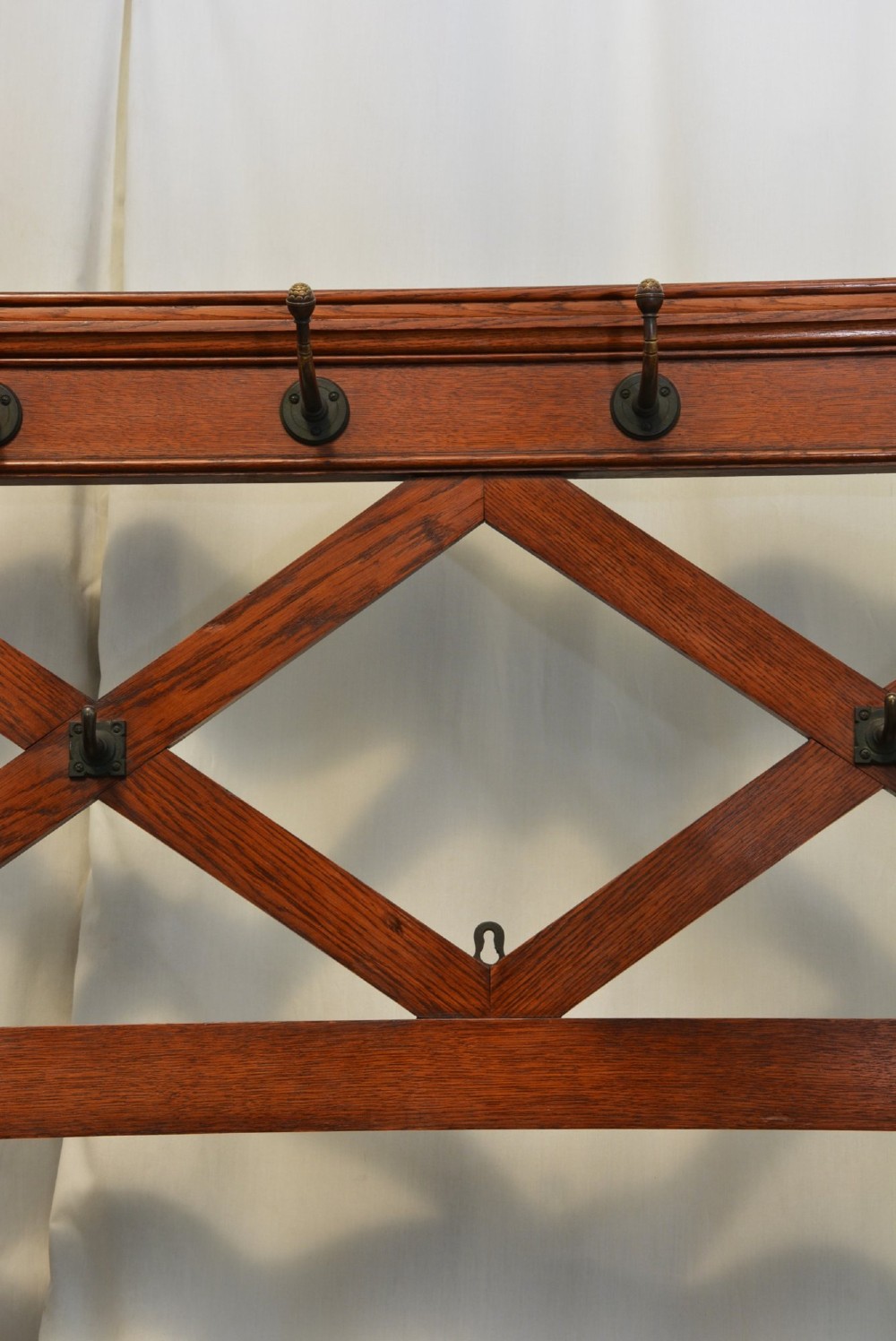 A Gothic Revival solid oak freestanding coat stand featuring upper hooks, carved diamond lattice fretwork, turned finials, and a shaped trestle base. View X