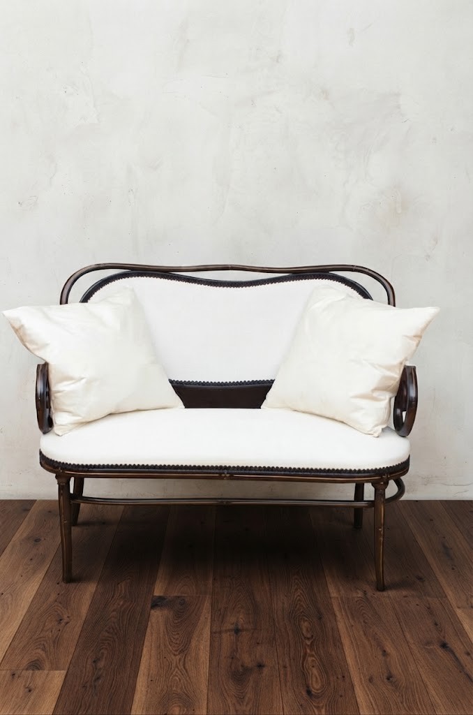 An ebonised steam-bent wood settee with a cream upholstered backrest and seat cushion.