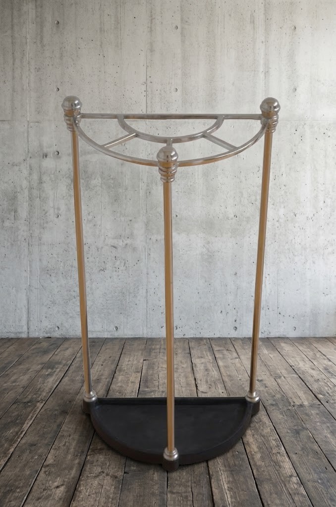 An Art Deco demi-lune nickel-plated umbrella stand featuring a semi-circular top frame with five divisions, vertical support rods with spherical finials, and a black cast iron drip tray base.