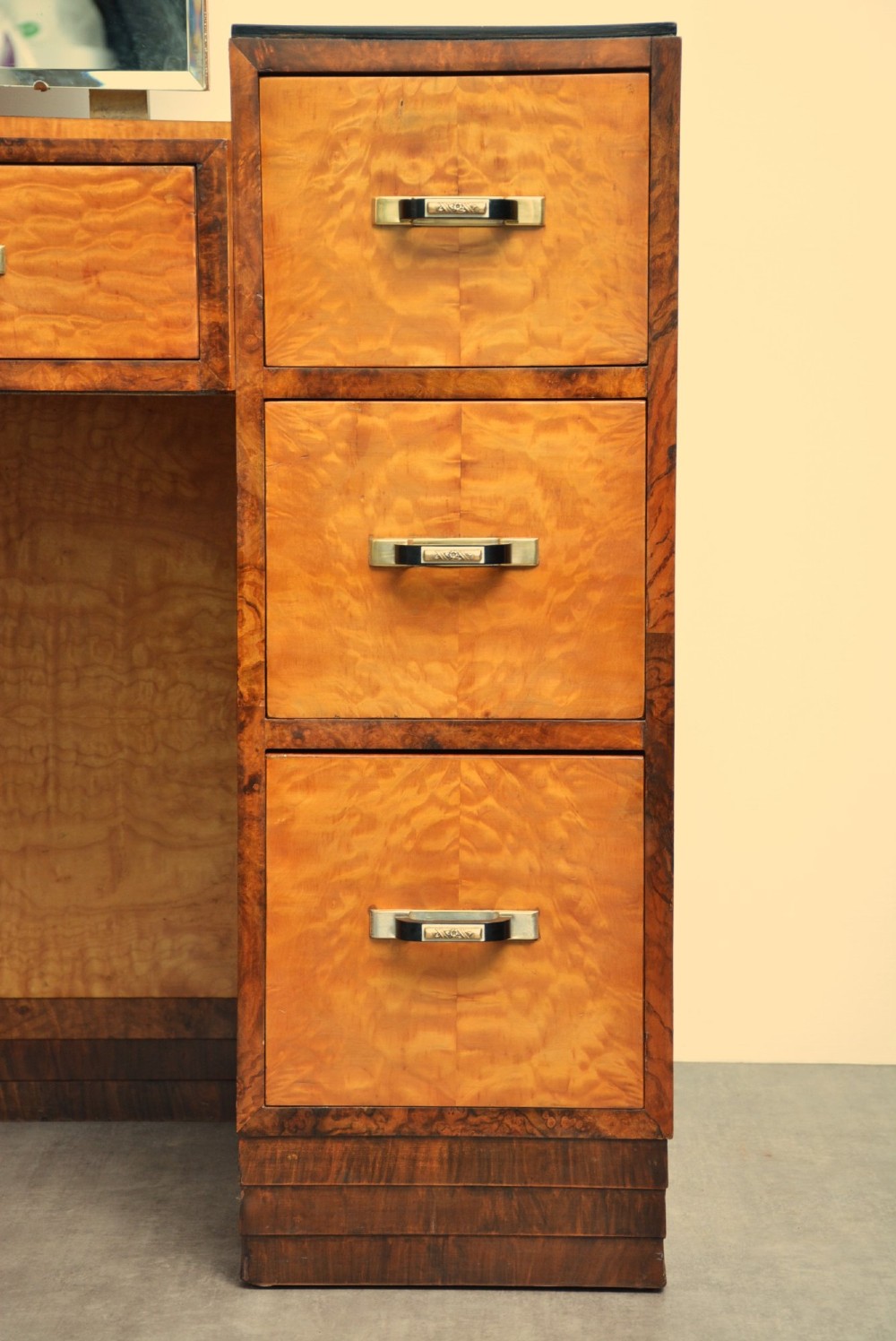An Art Deco asymmetrical dressing table crafted in burr maple veneer with an offset pedestal of drawers and a large frameless mirror. View X