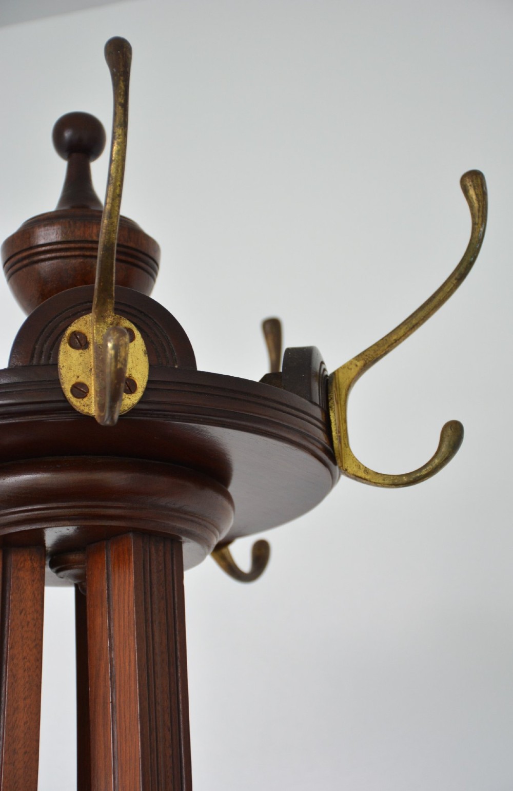 A tall antique walnut coat stand featuring a revolving top section with six brass hooks, a tapered central column, and four splayed feet. View IX