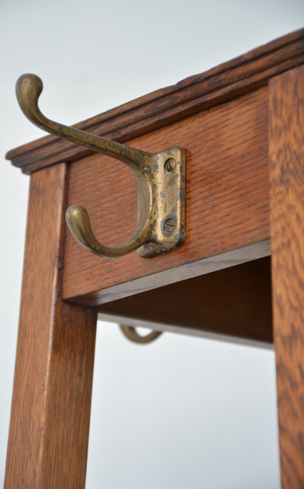 A tall, tapered solid oak Arts and Crafts coat stand featuring brass hooks at the top, a middle support bar, and a square drip tray at the base. View XII