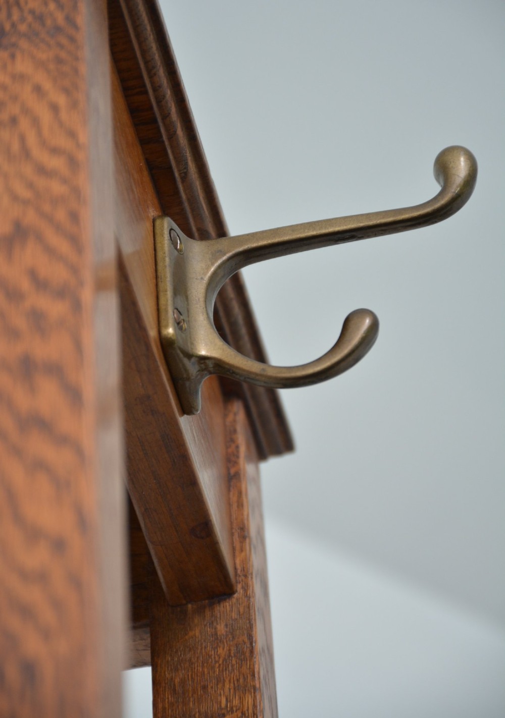 A tall, tapered solid oak Arts and Crafts coat stand featuring brass hooks at the top, a middle support bar, and a square drip tray at the base. View XIII
