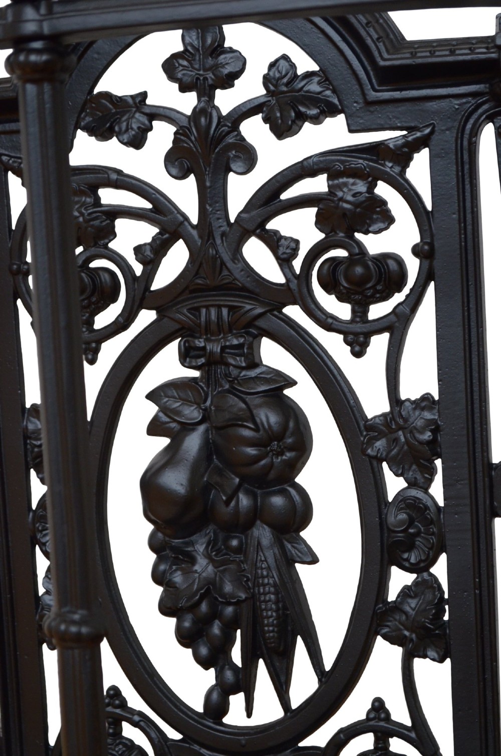 A black cast iron umbrella stand featuring an ornate foliate backplate, top support rail, and a twin-section drip tray at the base. View VI