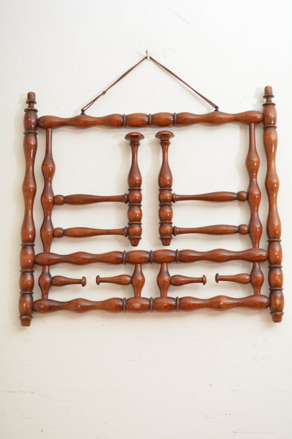 A French antique bobbin-turned wooden coat rack featuring swivelling upper hooks and fixed lower pegs suspended by a hanging cord. View V