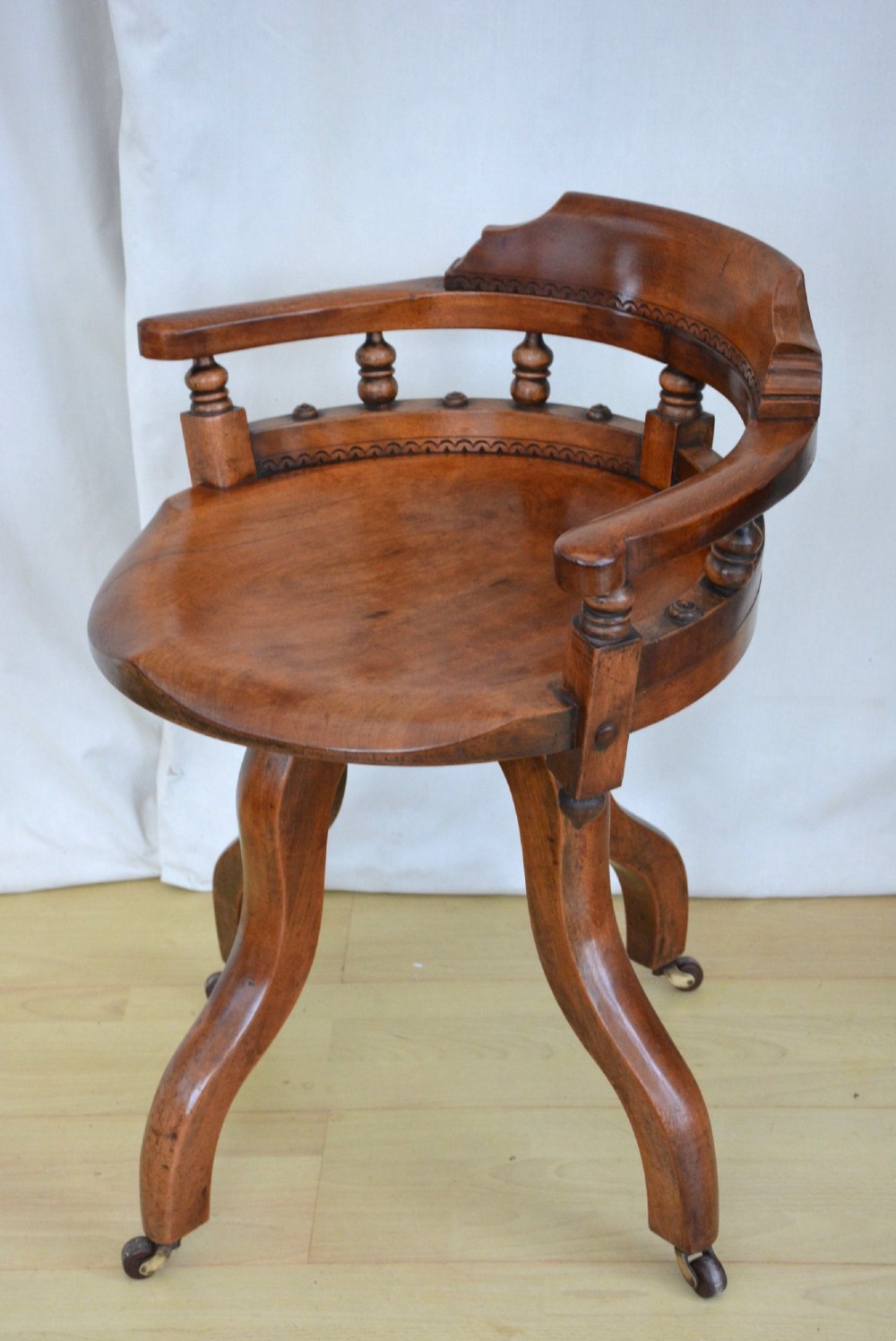 A 19th-century Victorian walnut revolving desk chair featuring a curved backrest with turned spindles, a contoured solid seat, and splayed legs on castors.