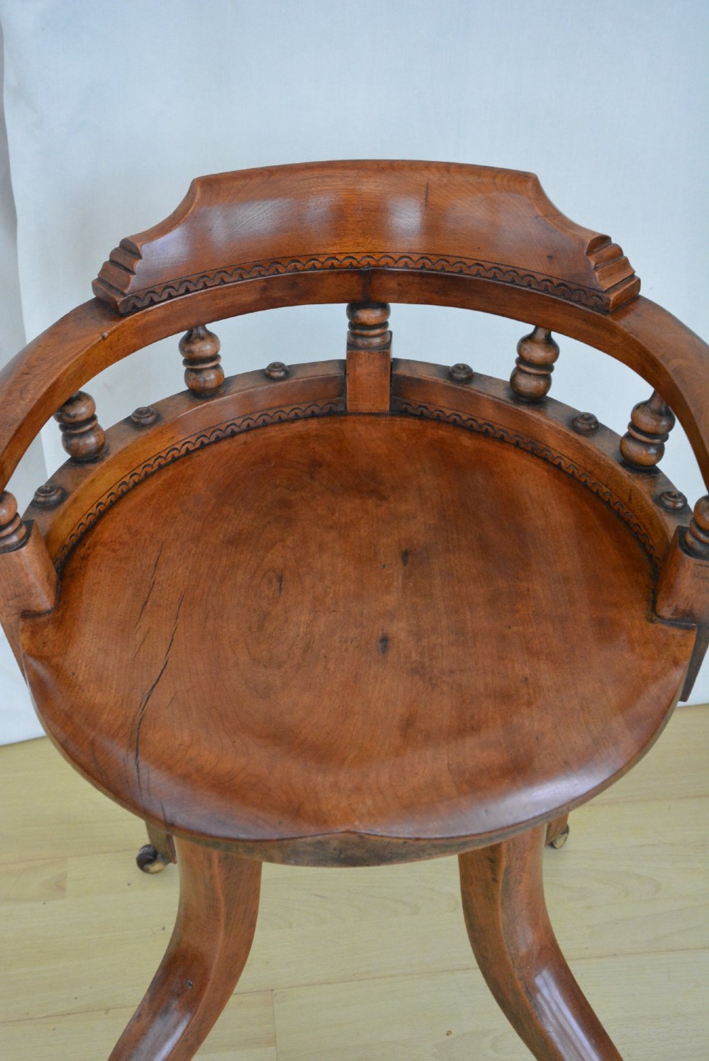 A 19th-century Victorian walnut revolving desk chair featuring a curved backrest with turned spindles, a contoured solid seat, and splayed legs on castors. View III