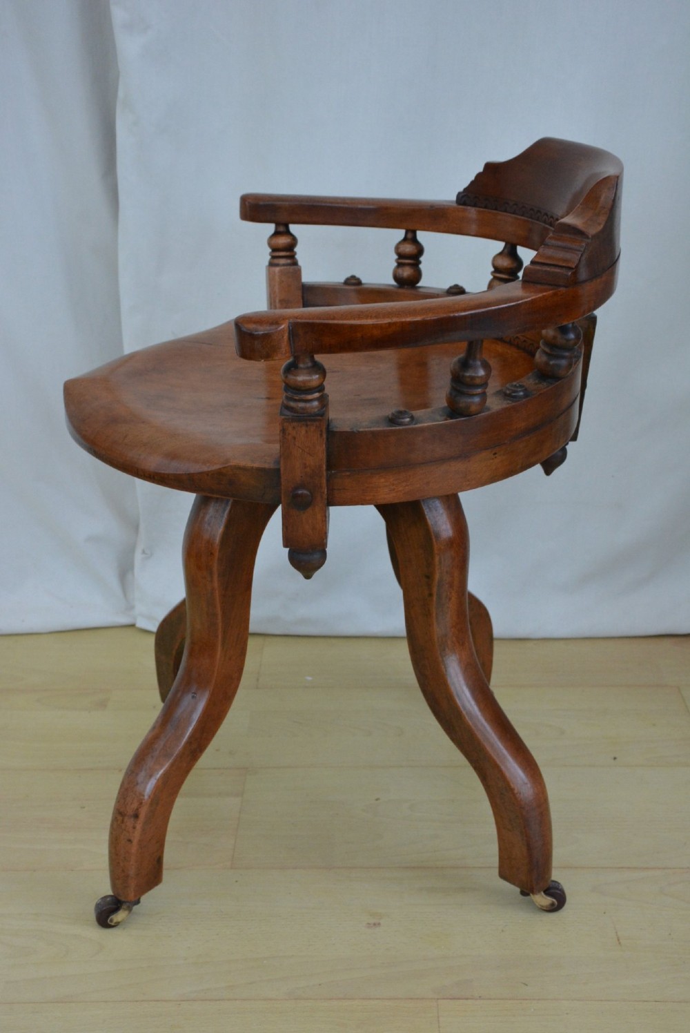 A 19th-century Victorian walnut revolving desk chair featuring a curved backrest with turned spindles, a contoured solid seat, and splayed legs on castors. View VI