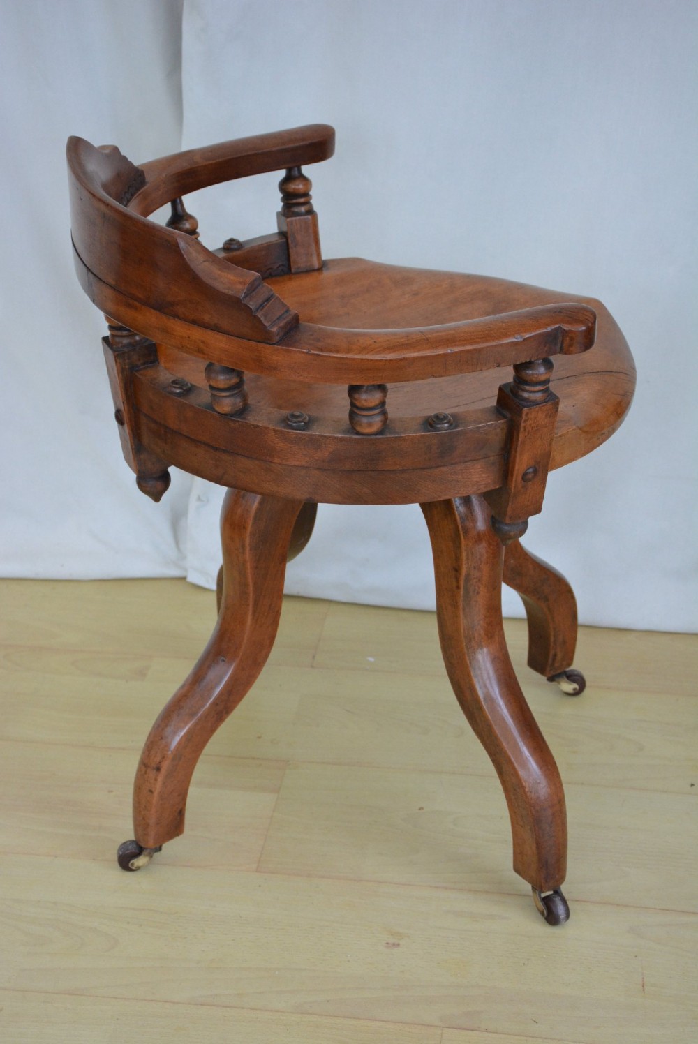 A 19th-century Victorian walnut revolving desk chair featuring a curved backrest with turned spindles, a contoured solid seat, and splayed legs on castors. View VII