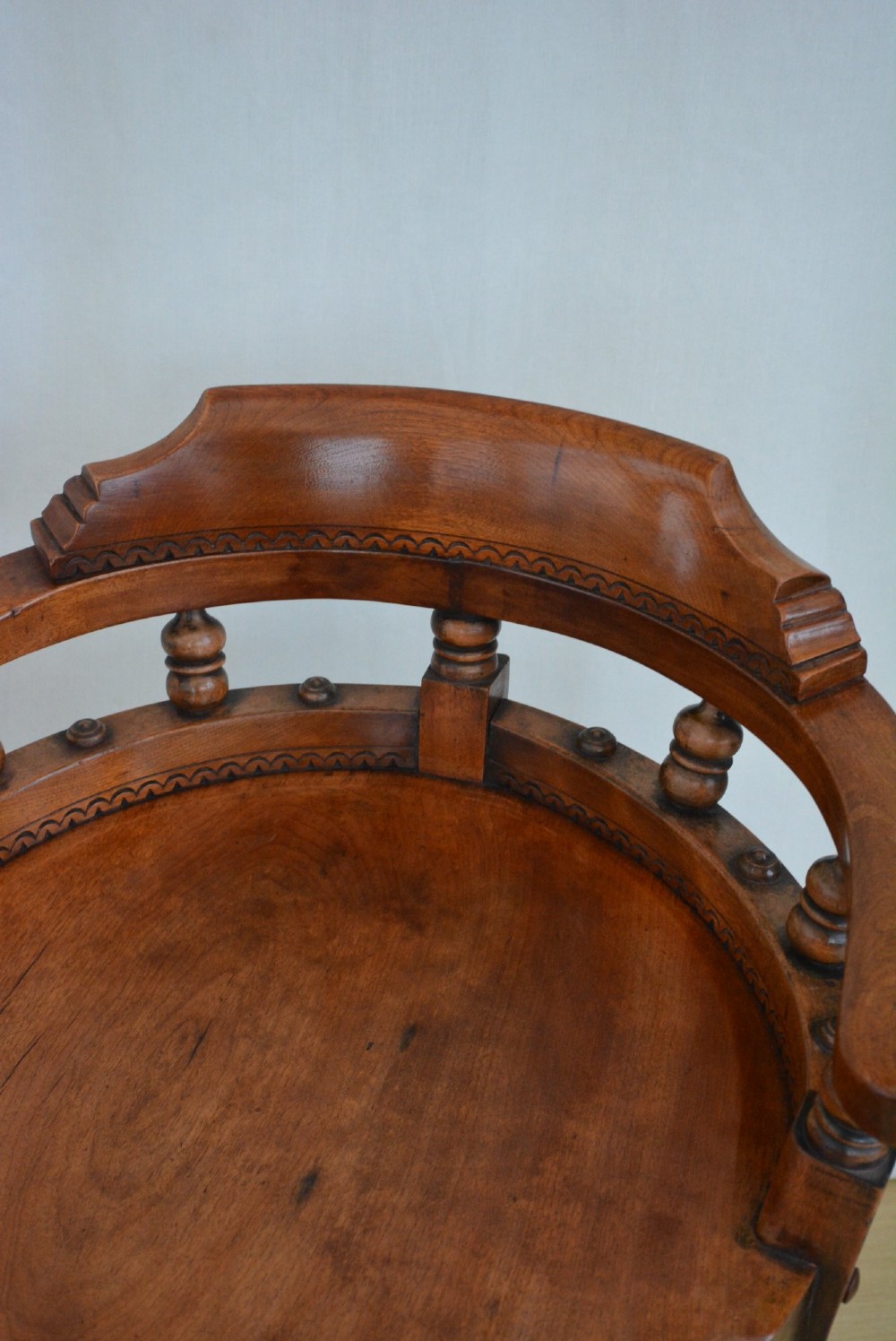 A 19th-century Victorian walnut revolving desk chair featuring a curved backrest with turned spindles, a contoured solid seat, and splayed legs on castors. View X