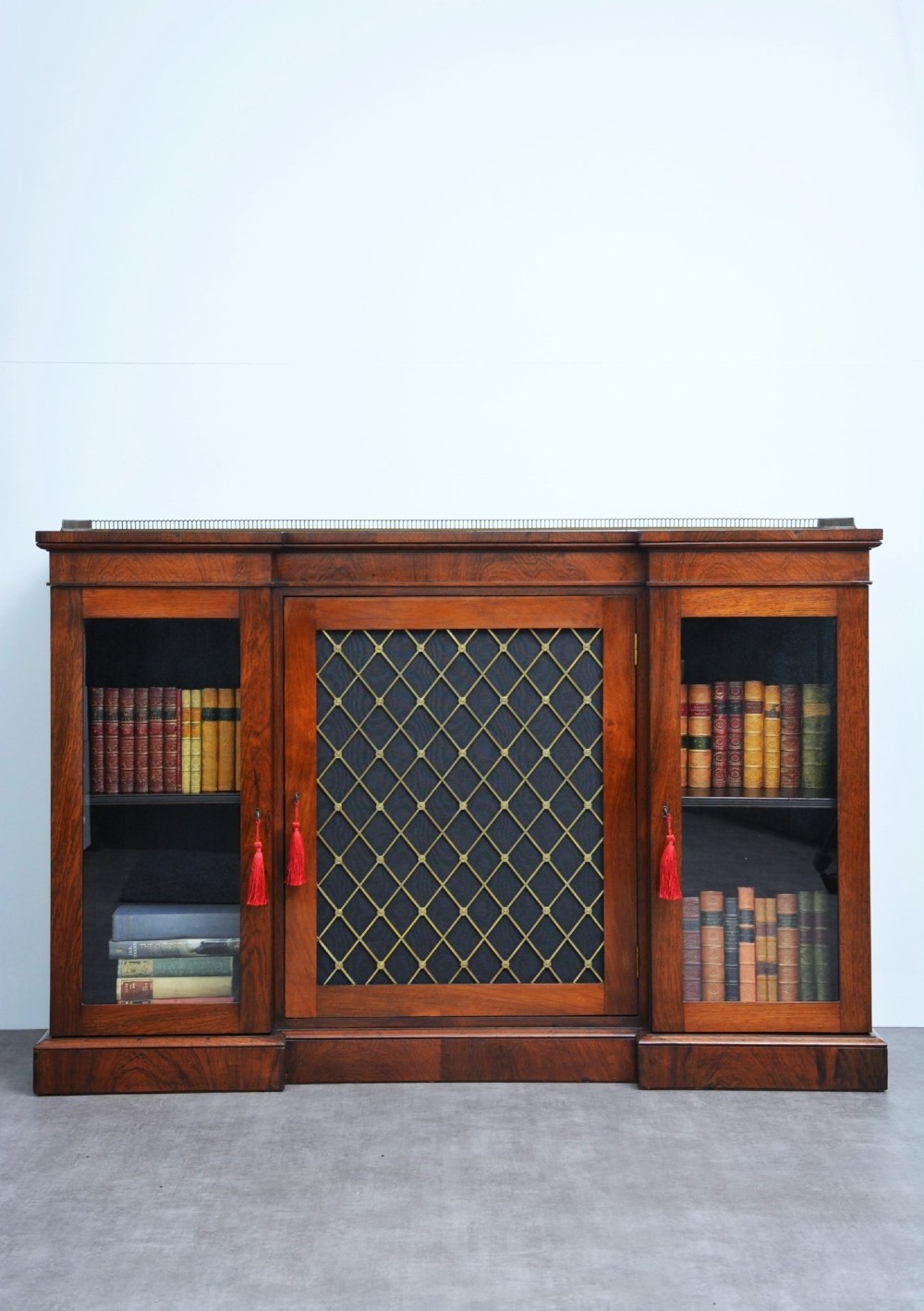 A low George IV rosewood cabinet bookcase featuring a central door with a brass wire mesh grille flanked by two glazed doors, topped with a brass gallery rail.