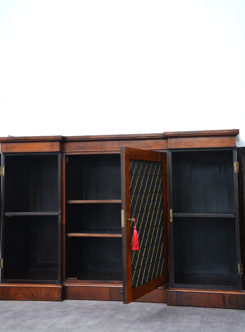 A low George IV rosewood cabinet bookcase featuring a central door with a brass wire mesh grille flanked by two glazed doors, topped with a brass gallery rail. View XI