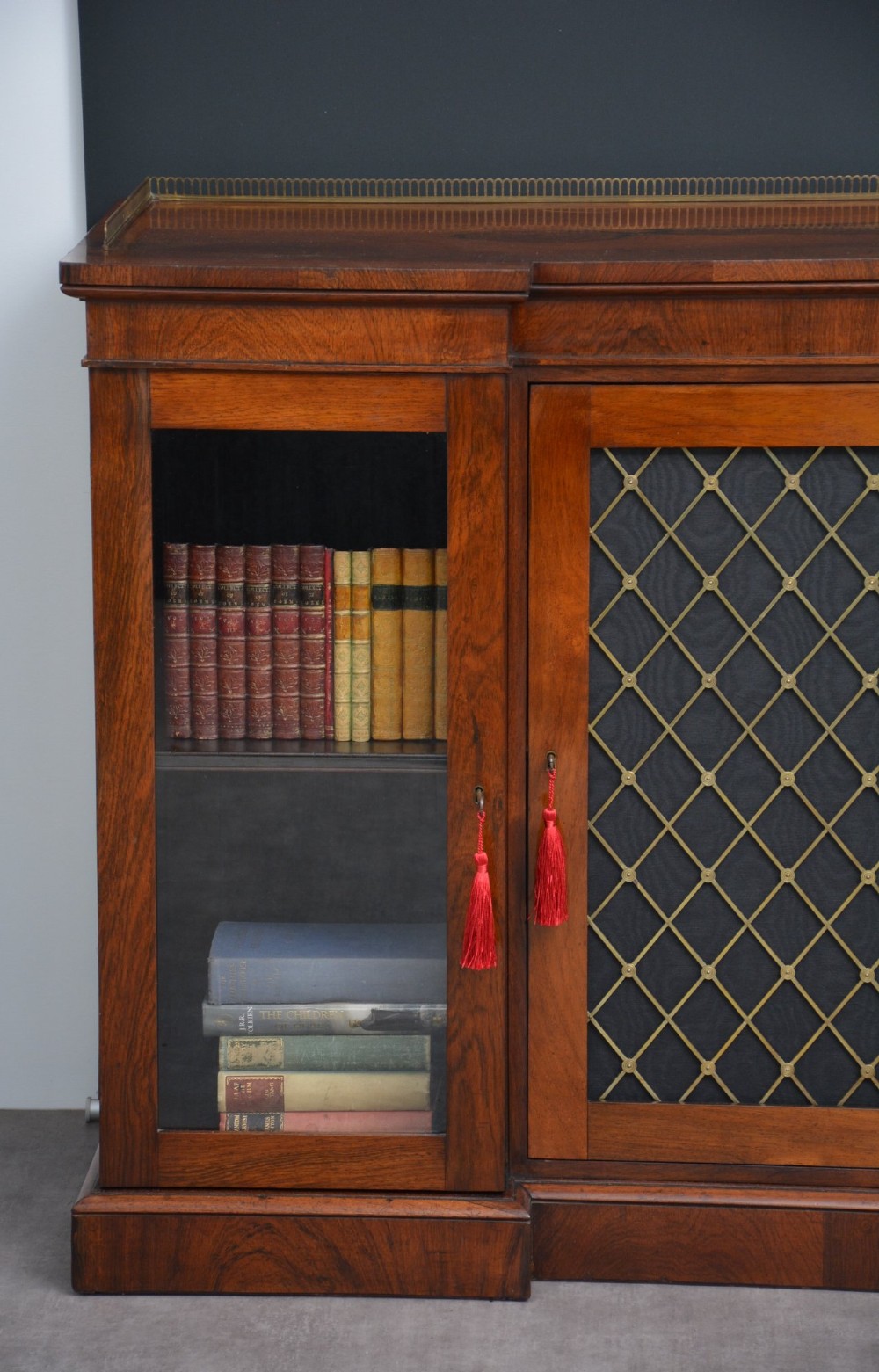 A low George IV rosewood cabinet bookcase featuring a central door with a brass wire mesh grille flanked by two glazed doors, topped with a brass gallery rail. View XII