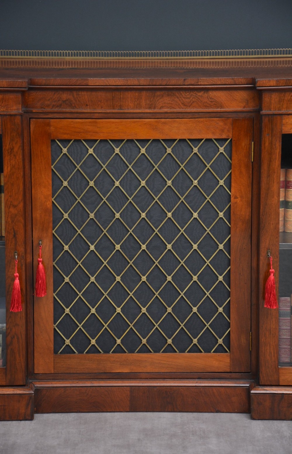 A low George IV rosewood cabinet bookcase featuring a central door with a brass wire mesh grille flanked by two glazed doors, topped with a brass gallery rail. View XIII