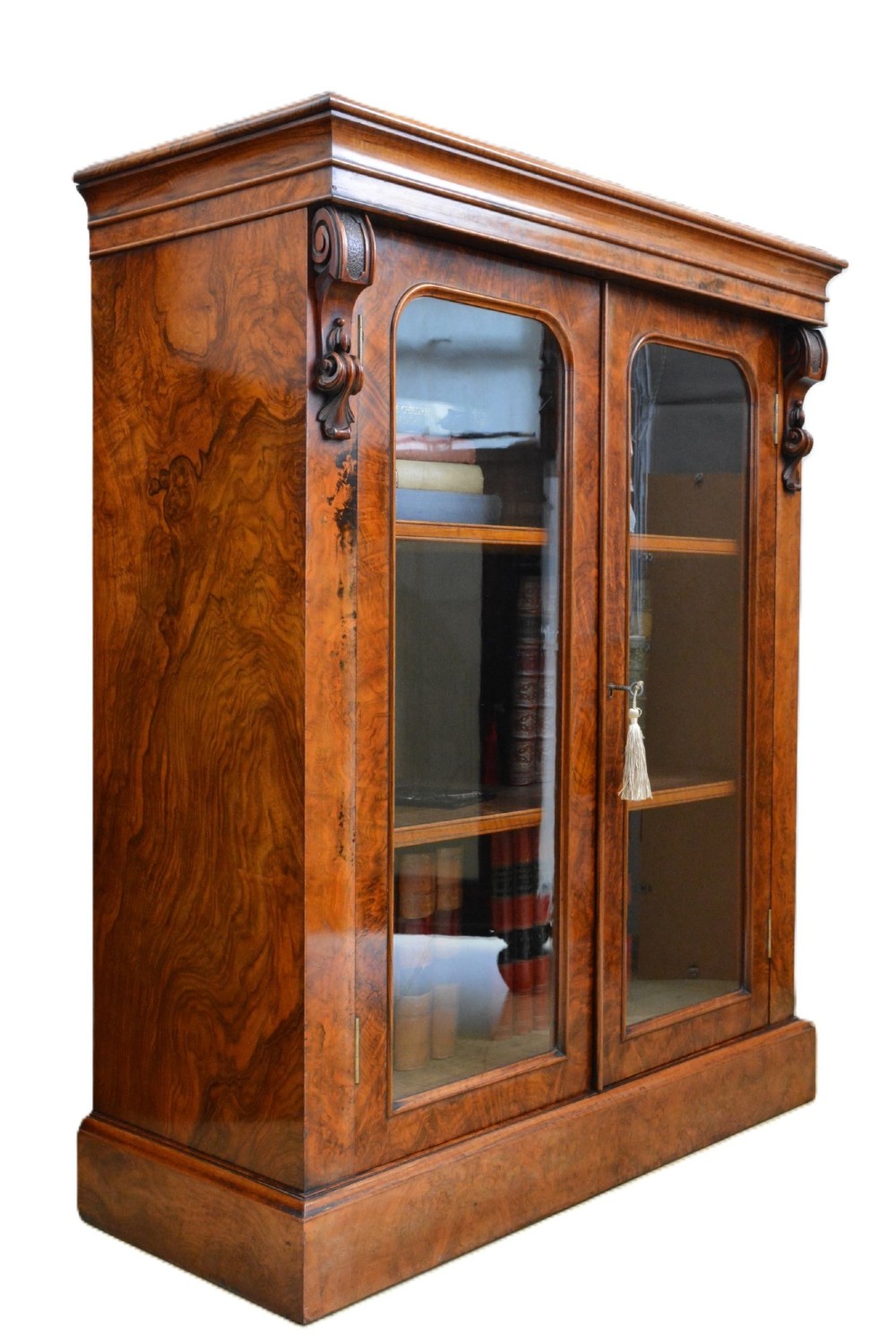 A Victorian figured walnut cabinet bookcase featuring two arched glazed doors, carved scroll corbels, and adjustable interior shelves. View II