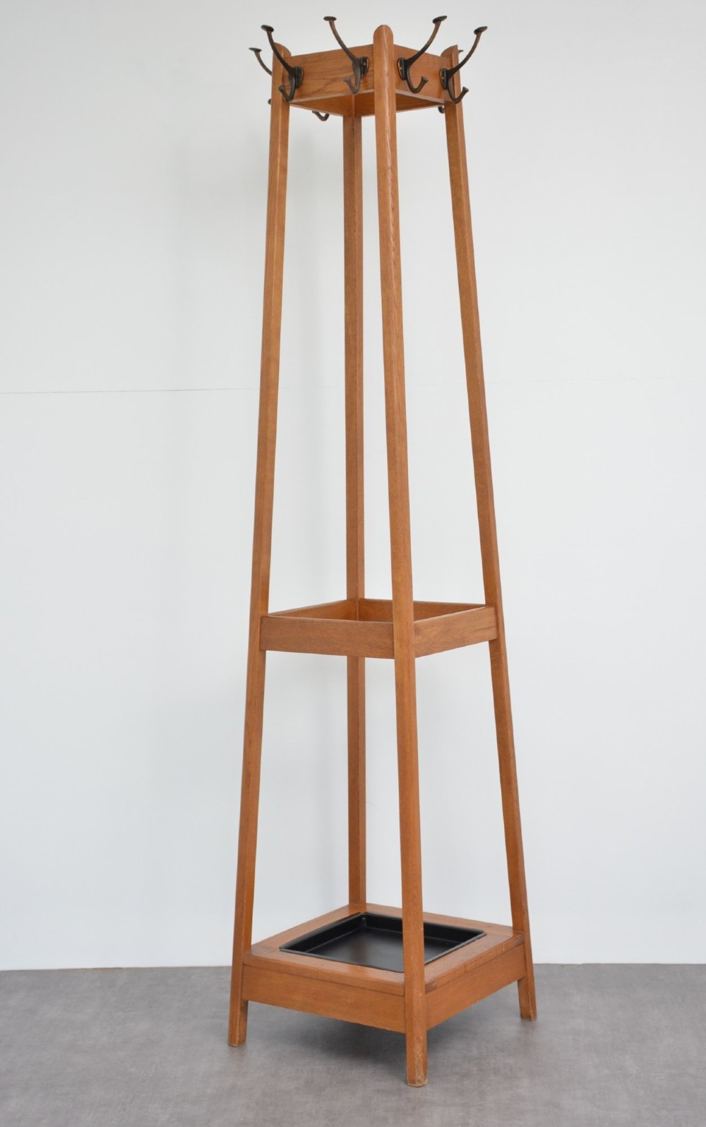 A tall square-framed oak coat stand featuring double metal hooks near the top, an intermediate retaining rail, and a square metal drip tray set into the timber base. View IX