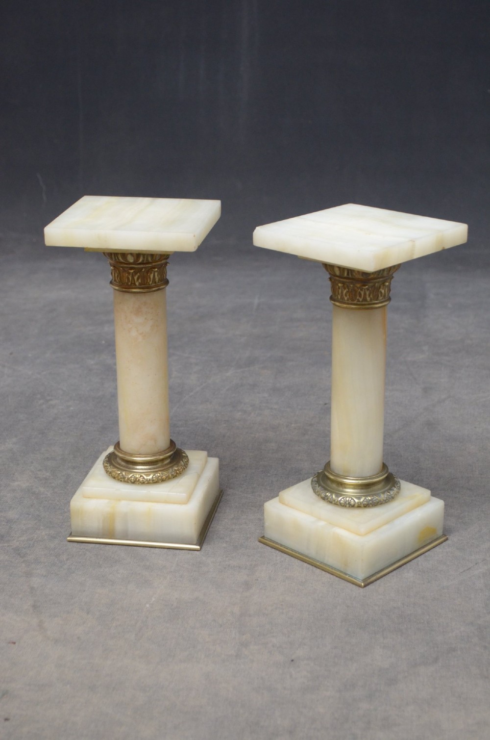 A pair of low Victorian cream onyx columns featuring ornate brass ormolu capitals and square tiered bases. View V