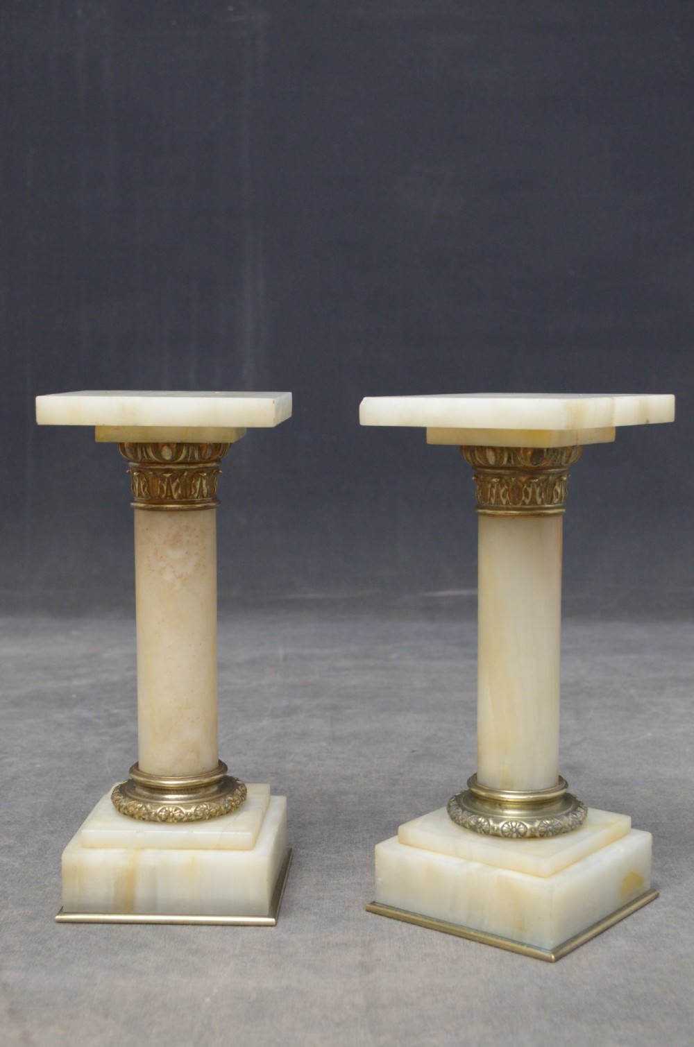 A pair of low Victorian cream onyx columns featuring ornate brass ormolu capitals and square tiered bases. View VI