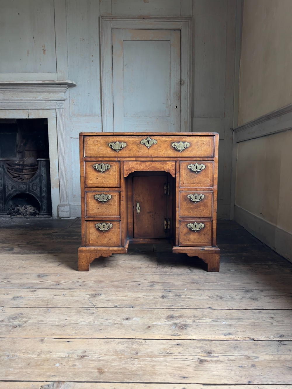 An 18th-century George II burr walnut kneehole desk featuring multiple drawers with brass handles, a central recessed cupboard, and bracket feet.