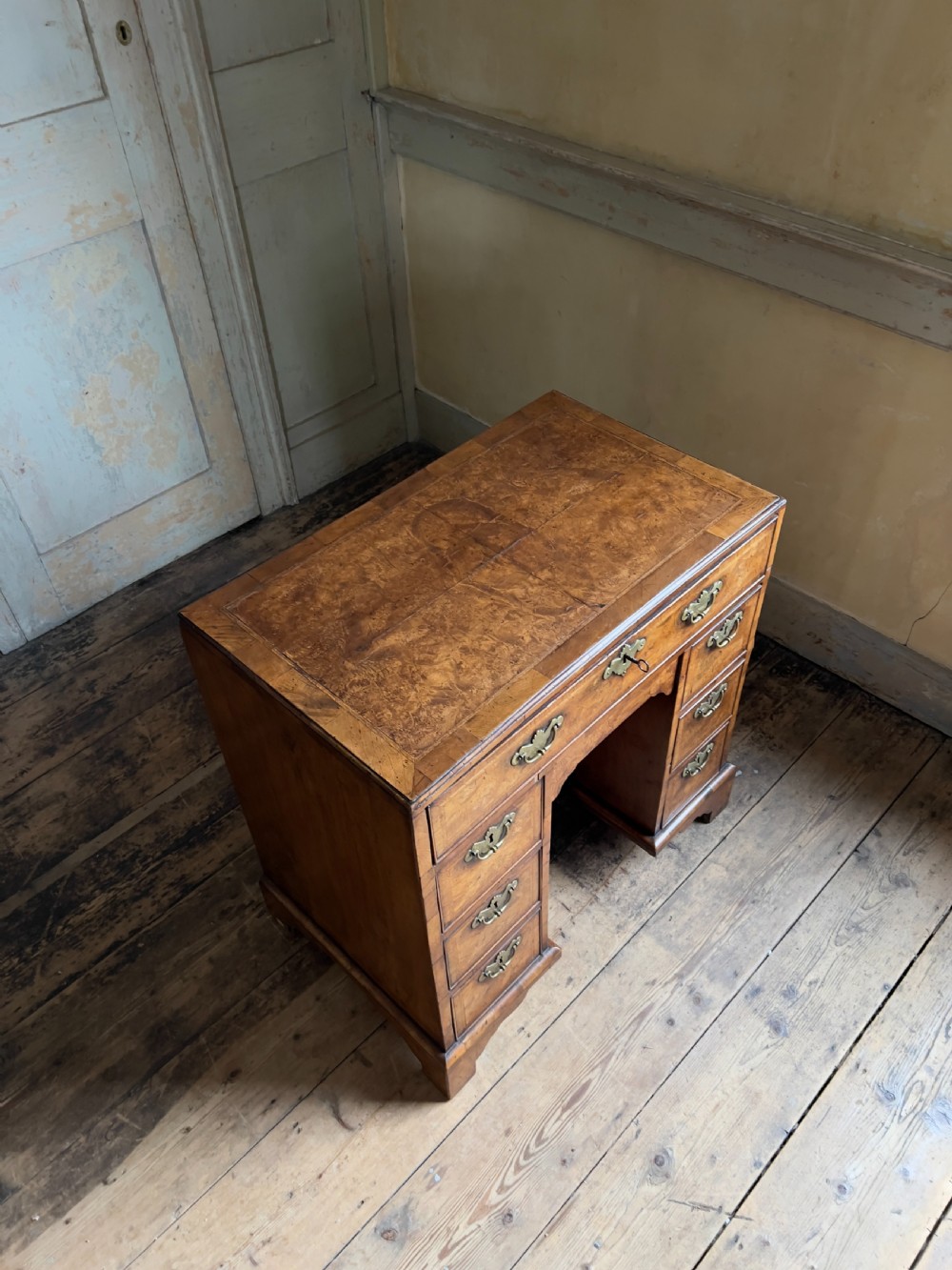 An 18th-century George II burr walnut kneehole desk featuring multiple drawers with brass handles, a central recessed cupboard, and bracket feet. View III